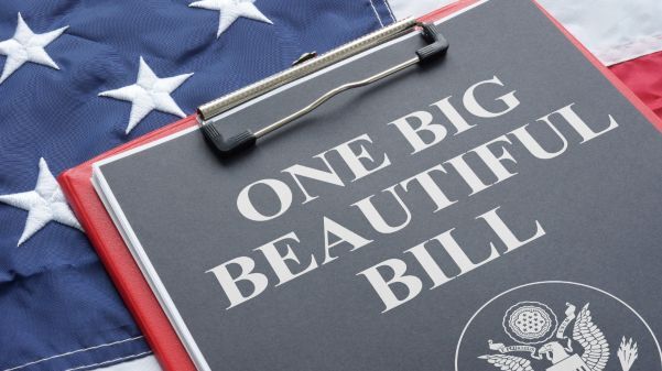 A clipboard labeled "One Big Beautiful Bill" rests on top of a U.S. flag; a government seal is visible at the bottom of the page.